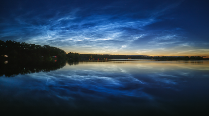 Noční svítící oblaky nad hladinou rybníku Hrádek z 5. července 2020. Nejčastěji se noční svítící oblaka (zkráceně NLC) vyskytují na severní polokouli v týdnech okolo letního slunovratu. Foto: Petr Horálek/FÚ v Opavě.